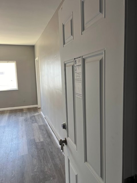 A white door with a handle is in the foreground of a room with a grey floor and walls.