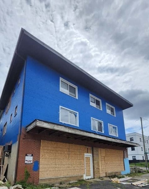 A blue building with a white door and windows is boarded up.