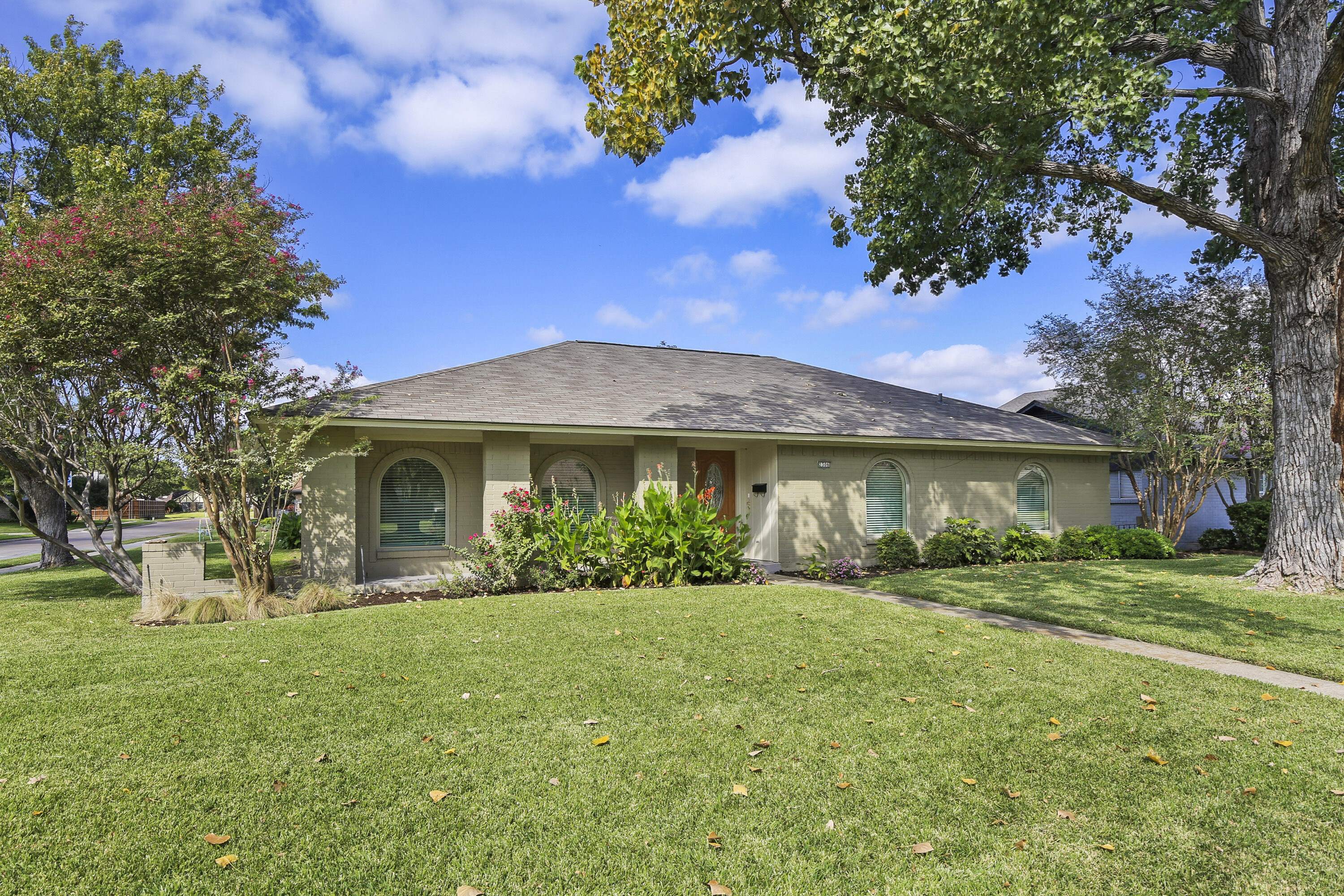 A house with a green lawn and trees in front.