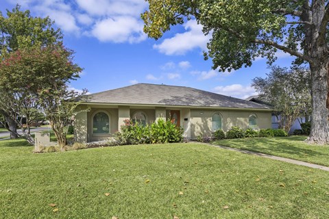 A house with a green lawn and trees in front.
