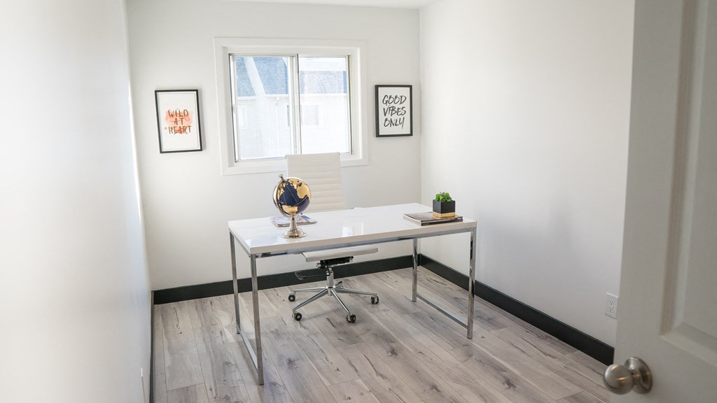 A white desk with a chair and a plant on it in a room with white walls.