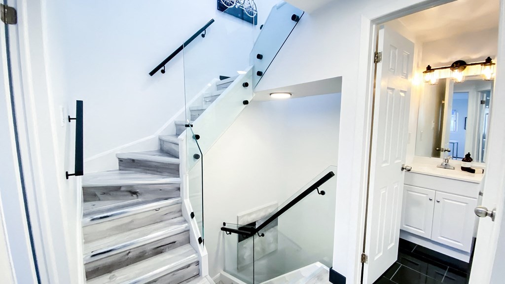 A white staircase with a glass railing and a white door leading to a bathroom.
