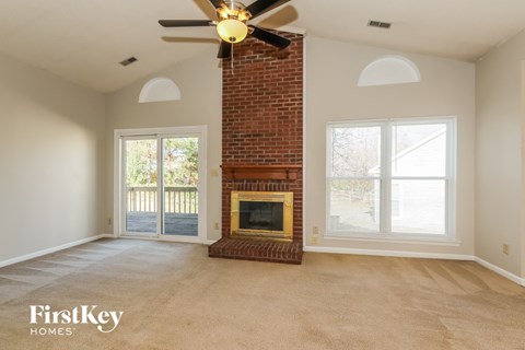 an empty living room with a brick fireplace and a ceiling fan