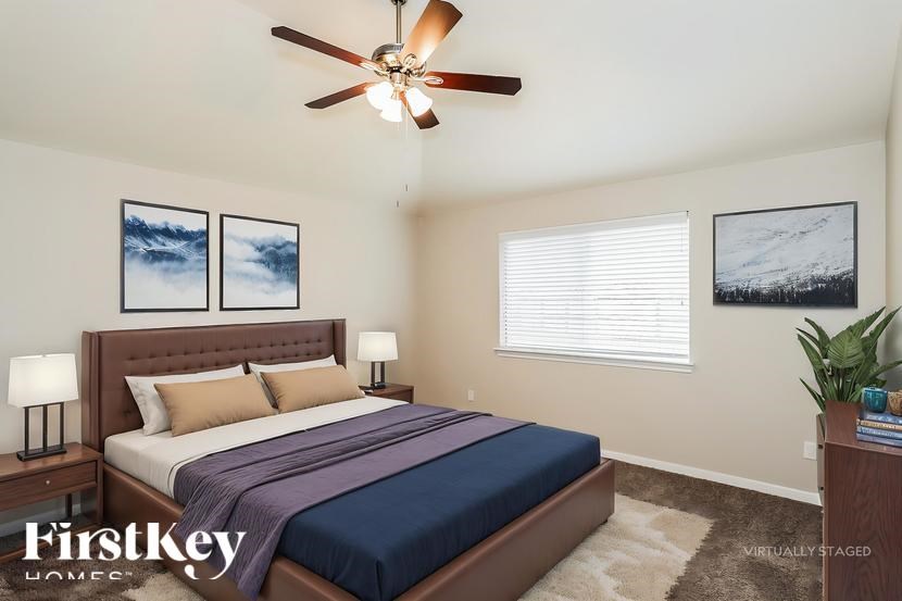A bedroom with a bed, two lamps, a ceiling fan, and two pictures on the wall.