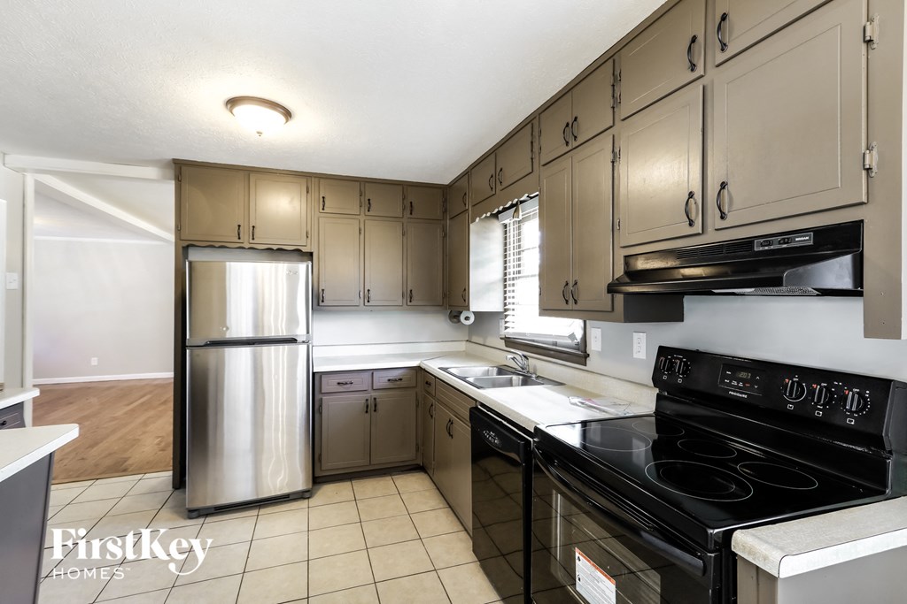 A kitchen with a stainless steel refrigerator and black stove top oven.