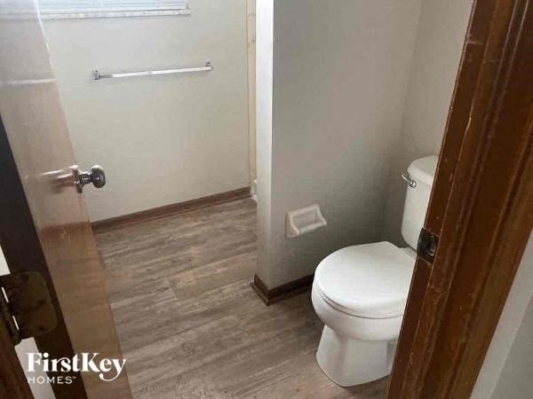 A white toilet in a bathroom with wood flooring and a white door.