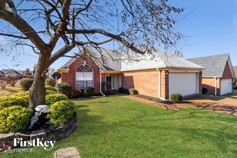 the front of a brick house with a yard and a tree