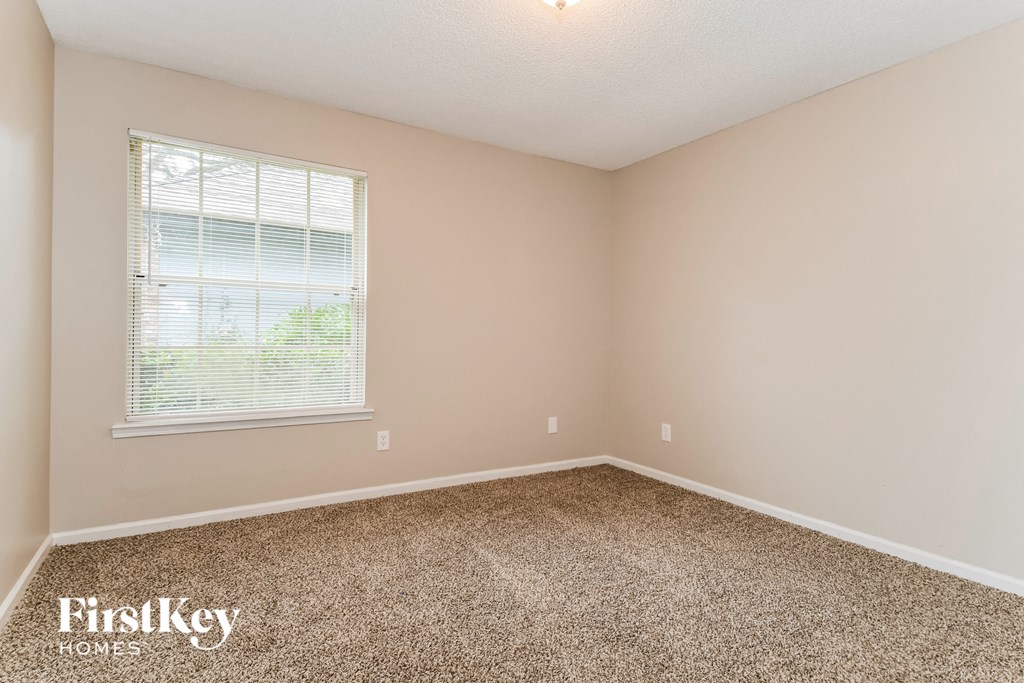 the spacious bedroom with carpeted flooring and a window