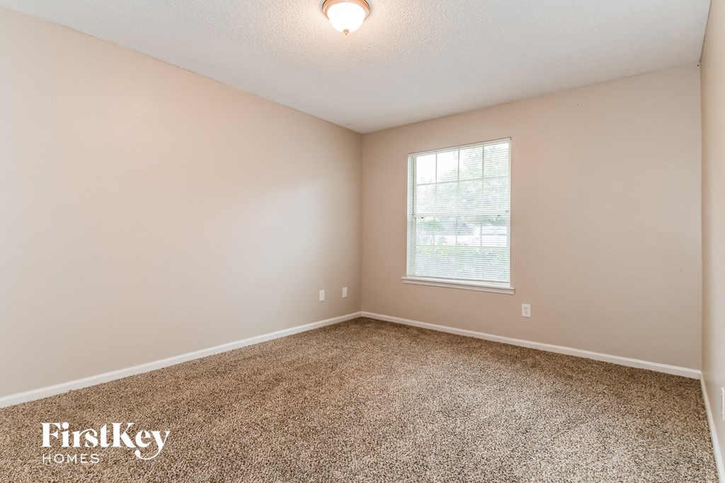 the spacious bedroom with carpeted flooring and a window