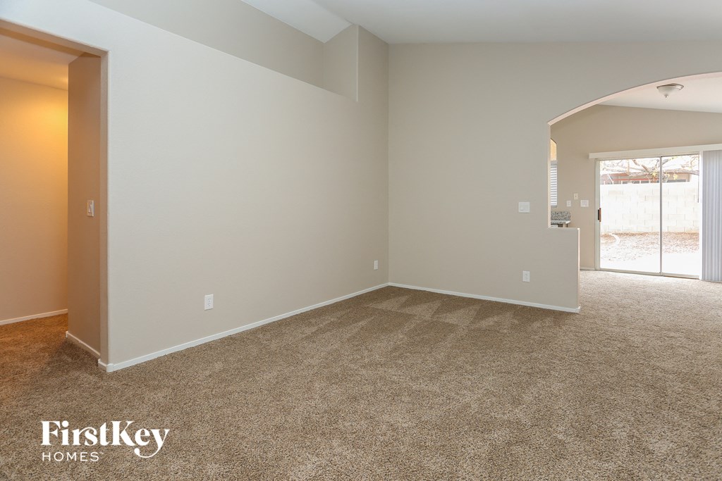 an empty living room with carpet and a door to the kitchen