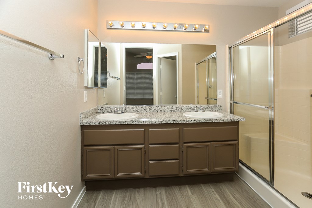 a bathroom with a counter with two sinks and a shower