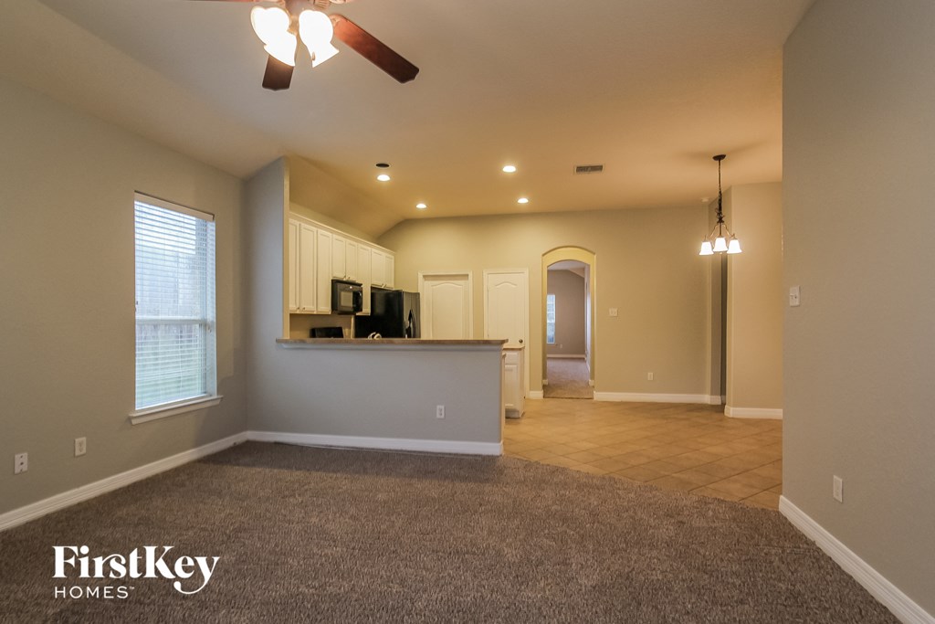 an empty living room with a kitchen and a ceiling fan