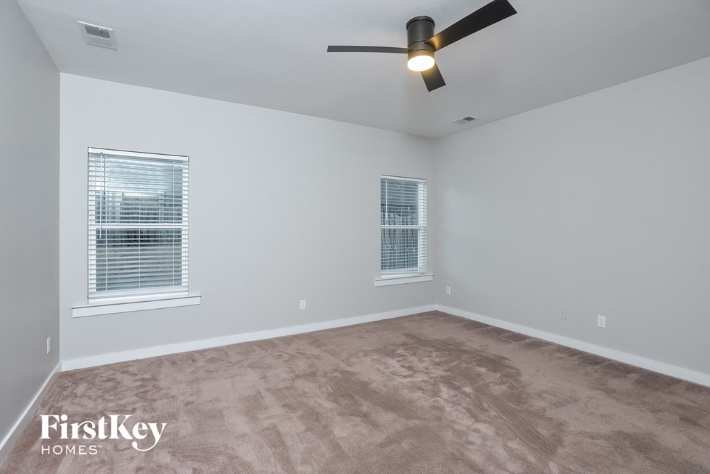 the living room of an empty home with carpet and a ceiling fan