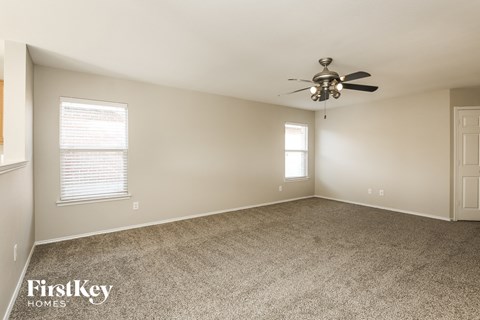 A spacious room with a ceiling fan and two windows.