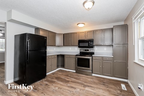 A kitchen with a black fridge and wooden floors.