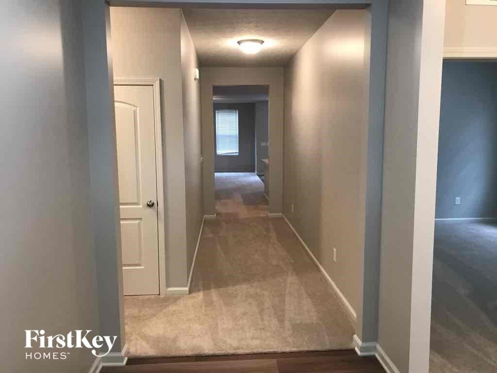 A hallway with a carpeted floor and a door on the left side.