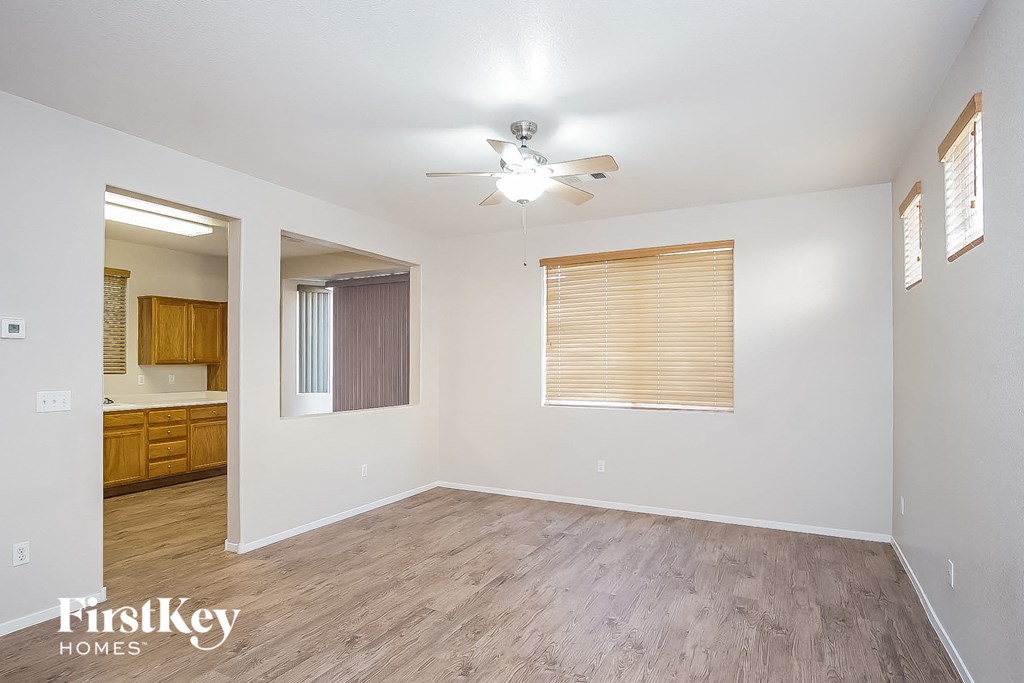 A room with a ceiling fan and light, wooden floors, and a window with blinds.