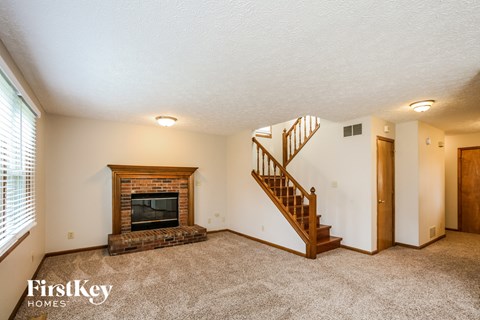 A spacious living room with a fireplace and a staircase.