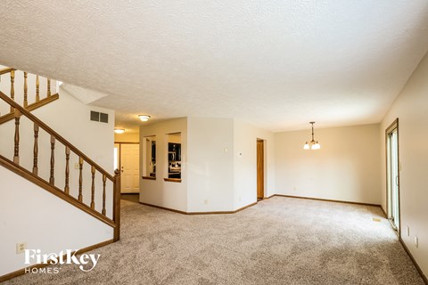 A spacious living room with a staircase on the left side and a chandelier hanging from the ceiling.