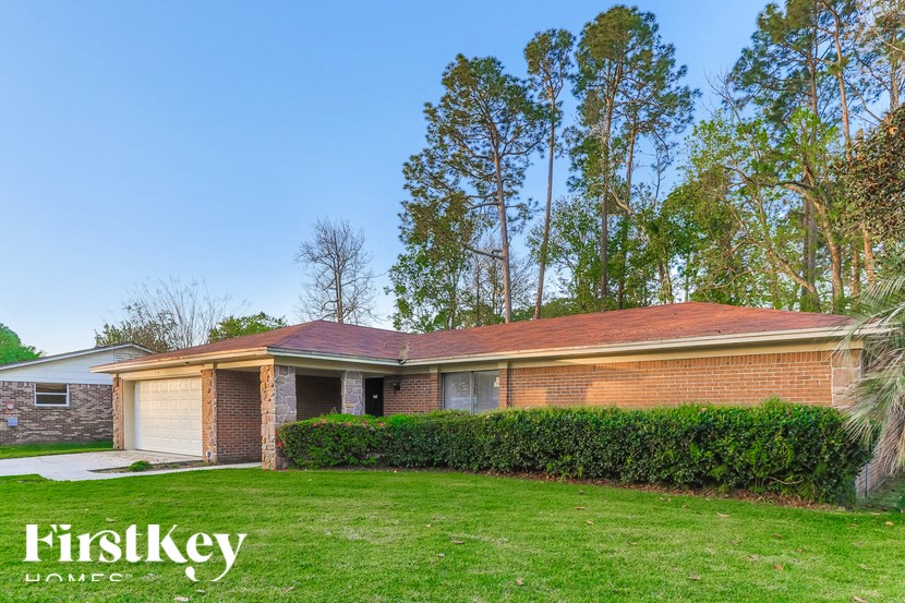 A house with a brick exterior and a garage is surrounded by a green lawn and trees.