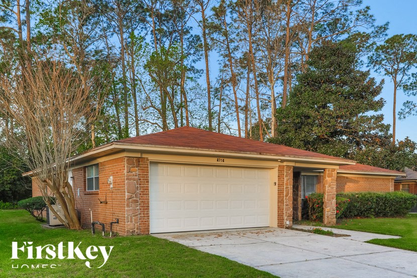 A brick house with a garage door and a tree in front of it.