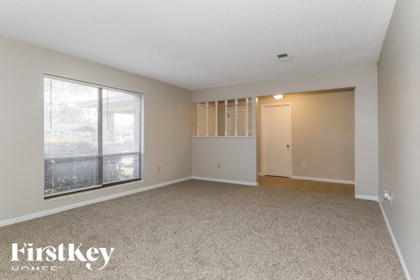 A spacious room with a carpeted floor and a large window with blinds.