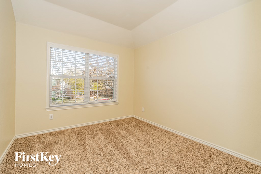 A room with a carpeted floor and a window showing a view of trees and a house.