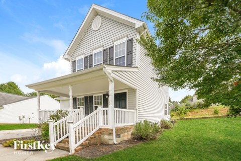 A house with a porch and a tree in front of it.