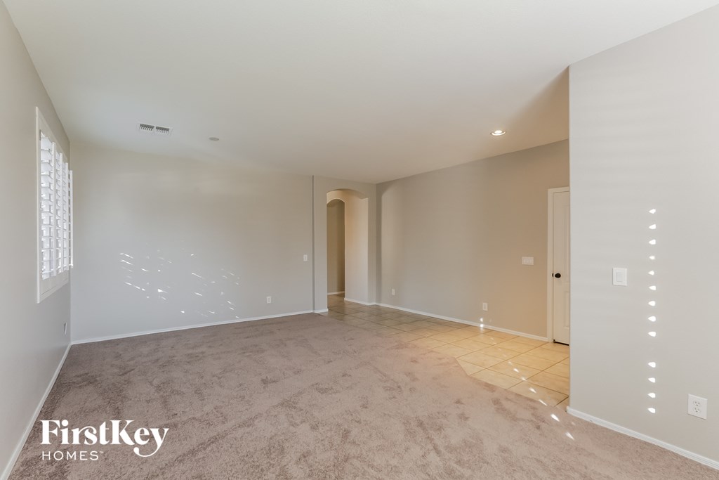A spacious, empty room with a carpeted floor and white walls, with a doorway leading to another room.