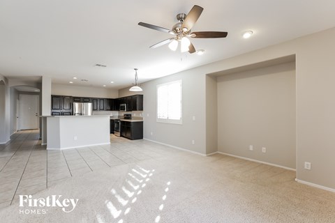 A spacious living room with a ceiling fan and a kitchen area in the background.