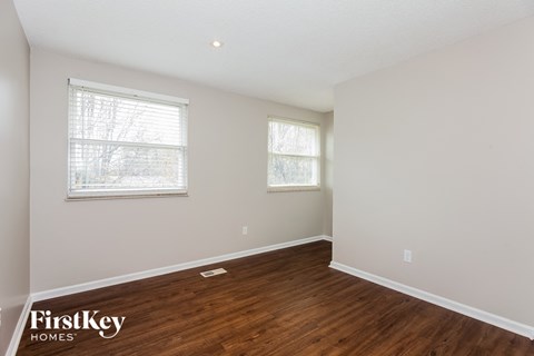 a bedroom with white walls and wood flooring and two windows