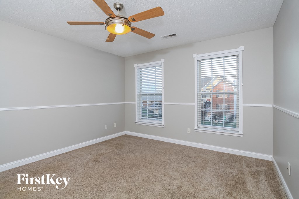 an empty room with a ceiling fan and two windows