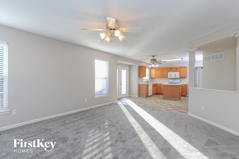 A spacious living room with a kitchen in the background and a carpet on the floor.