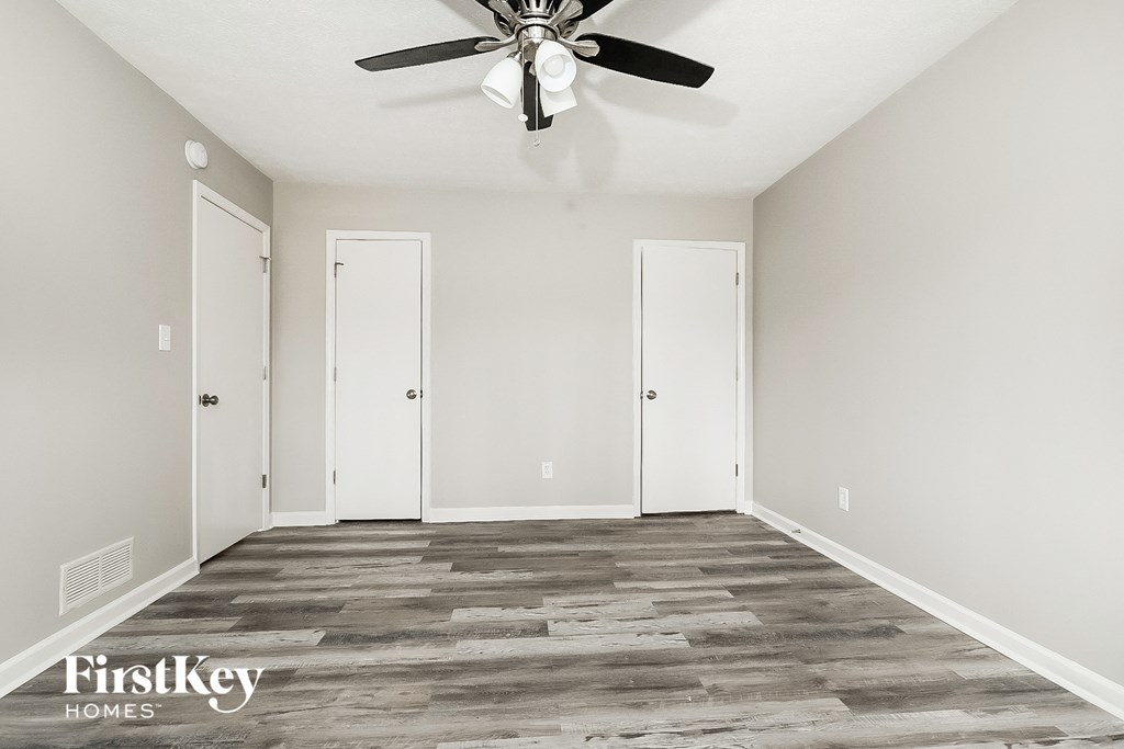 A room with a ceiling fan and three doors.