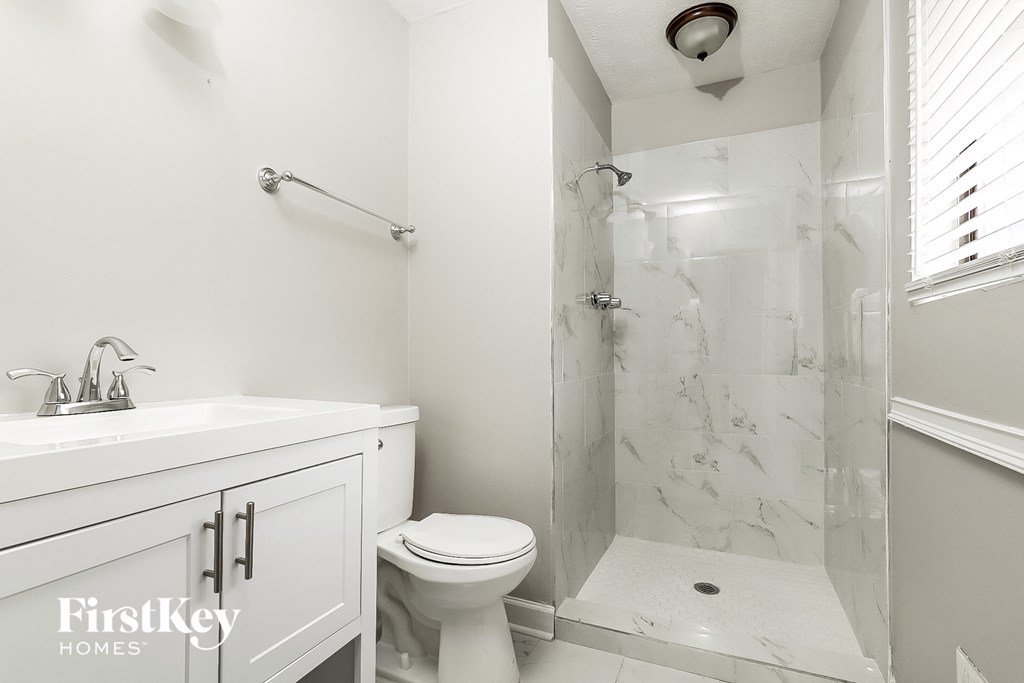 A white bathroom with a marble shower and toilet.