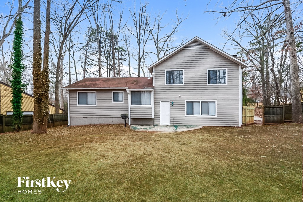 A house with a brown roof and a grey siding is surrounded by trees.