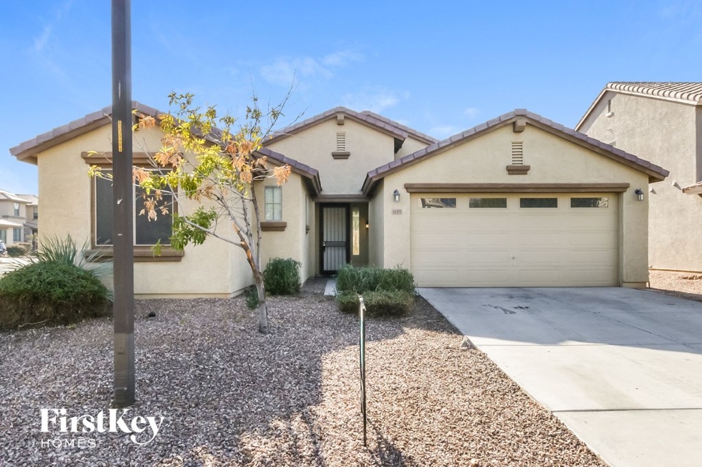 a beige house with a white garage door and a gravel driveway