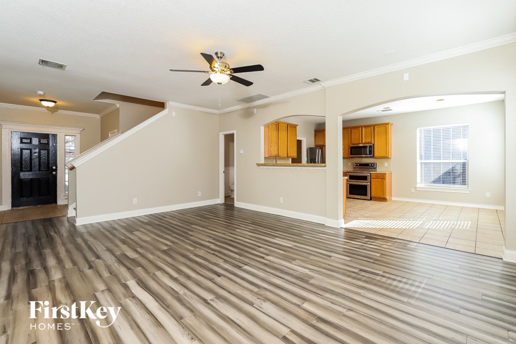 an empty living room with a ceiling fan and a kitchen