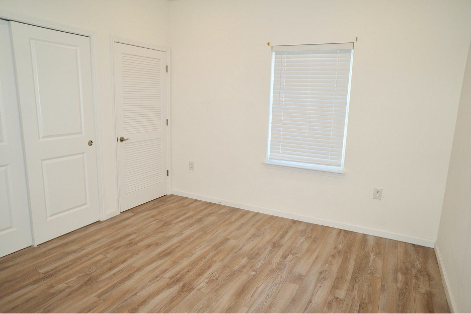 a bedroom with white walls and wood floors and a window