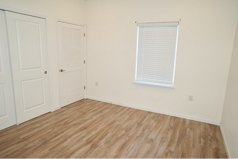 a bedroom with white walls and wood floors and a window