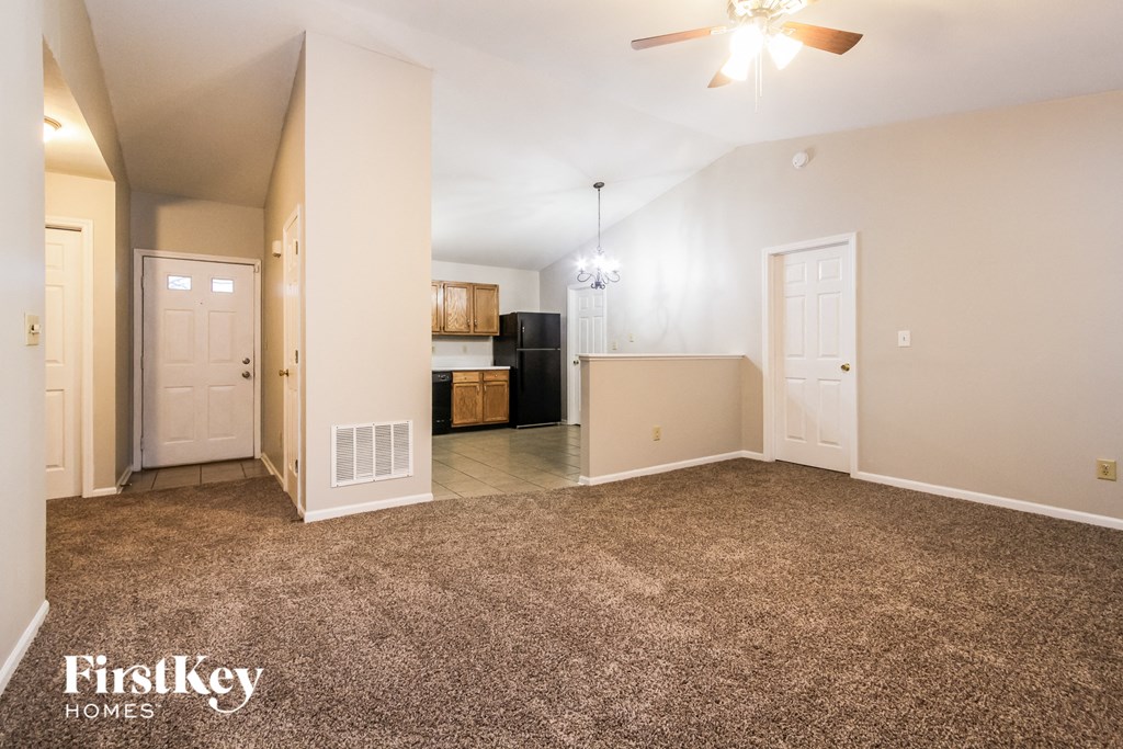 an empty living room with a carpeted floor and a kitchen