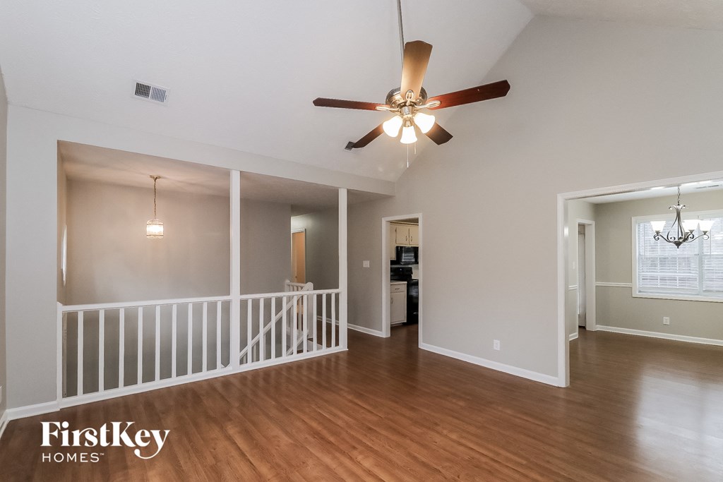an empty living room with a ceiling fan and a staircase