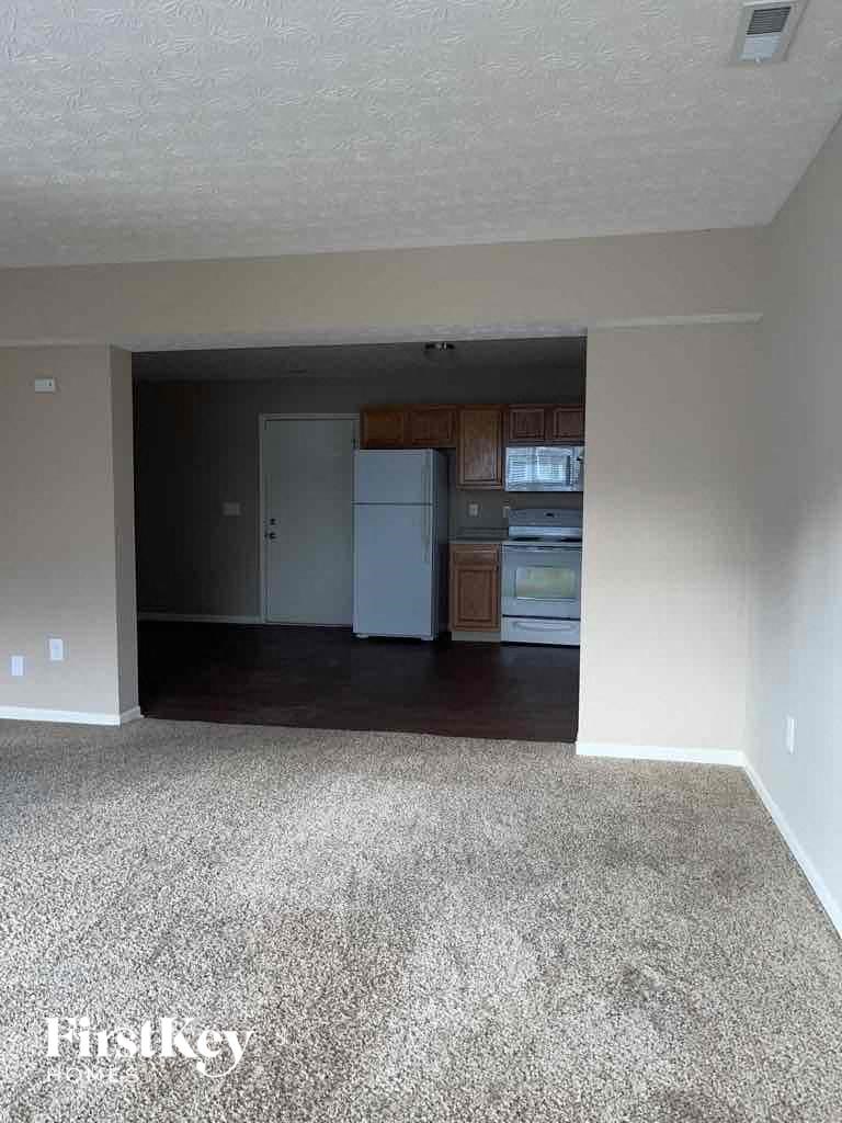 A room with a carpeted floor and a kitchen area in the background.