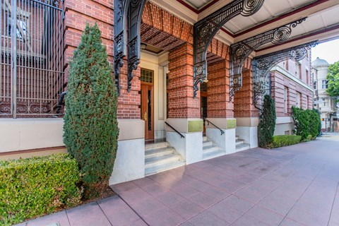 A red brick building with a black iron gate and a green tree.