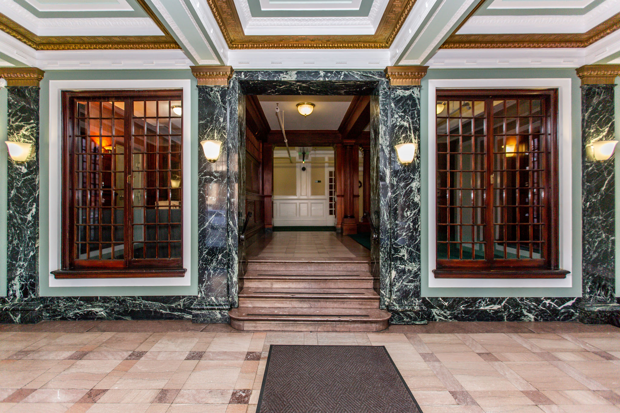 A hallway with marble floors and walls, and wooden doors.