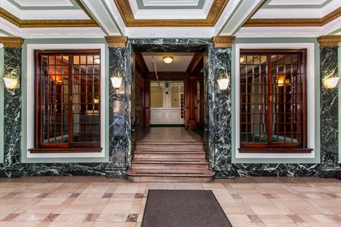 A hallway with marble floors and walls, and wooden doors.