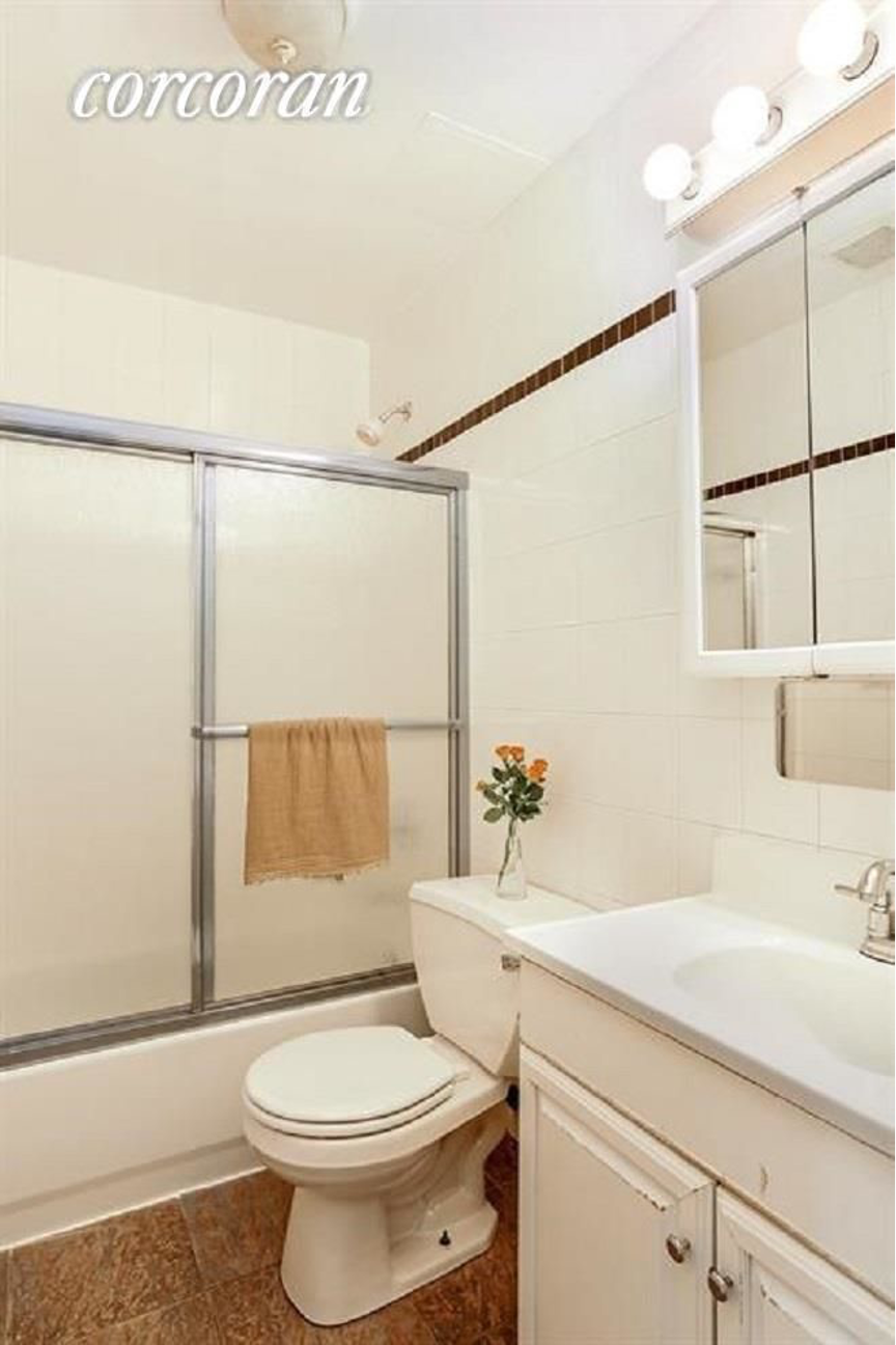 A white toilet sits in a bathroom with a white sink and a brown towel hanging on the glass shower door.