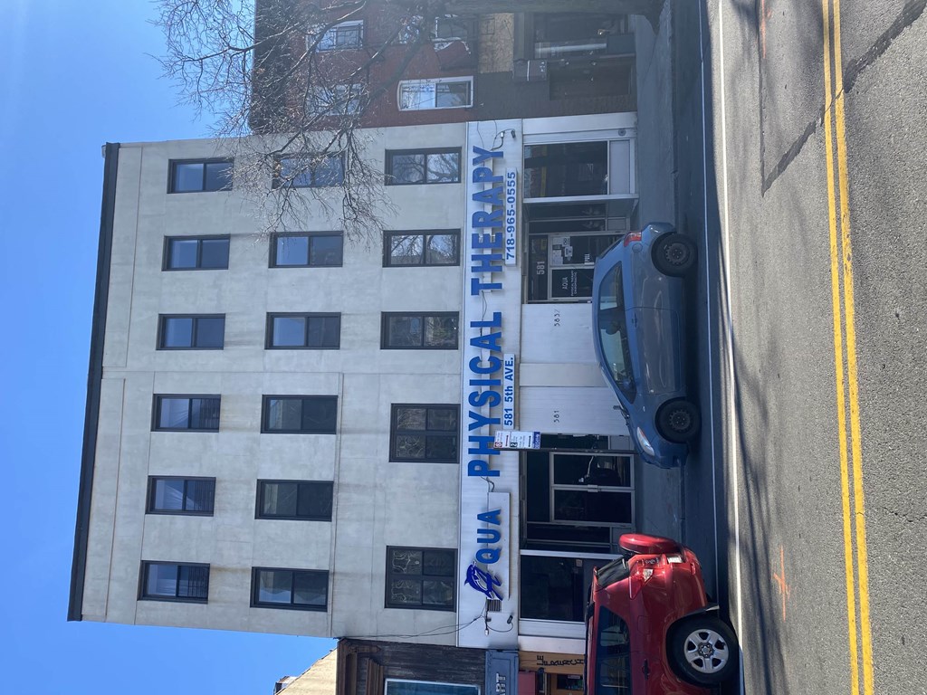 A white truck with a blue and white sign that says "QUA PHYSICAL THERAPY" is parked on the side of a street.
