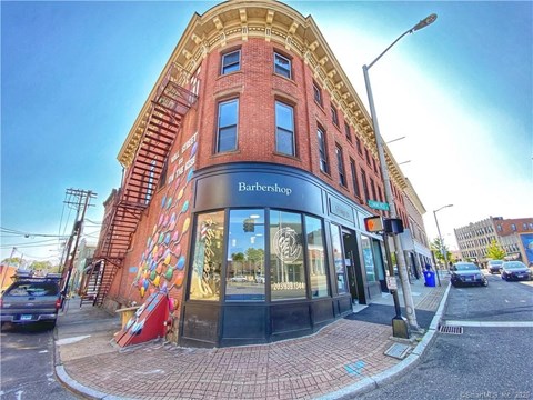A street view of a Barbershop with a red brick building and a mural on the side.