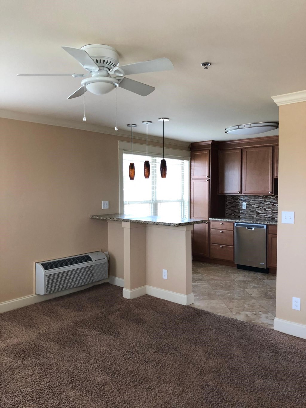 an empty living room with a kitchen and a ceiling fan
